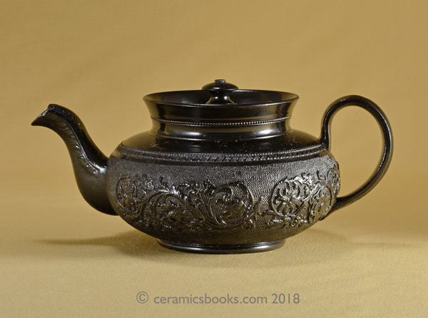 Small low-round black basalt teapot with floral sprig frieze on gauze background, marked CYPLES. AP/1005