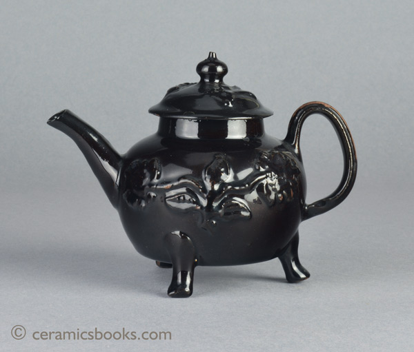 Shining Black 'Jackfield' type teapot on 3 feet with applied vine leaf and flower sprigs c.1755-1765. Obverse profile. AP/1240.