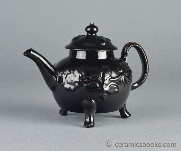 Shining Black 'Jackfield' type teapot on 3 feet with applied vine leaf and flower sprigs c.1755-1765. Obverse. AP/1240.