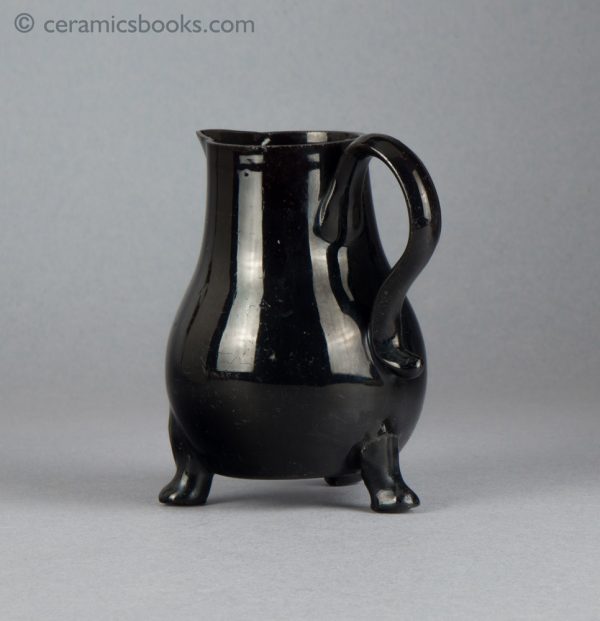 Small black-glazed 'Jackfield' type jug on three feet, with sparrow-beak spout. c.1755-1765. Back obverse.