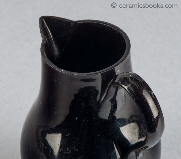 Small black-glazed 'Jackfield' type jug on three feet, with sparrow-beak spout. c.1755-1765. Rim.
